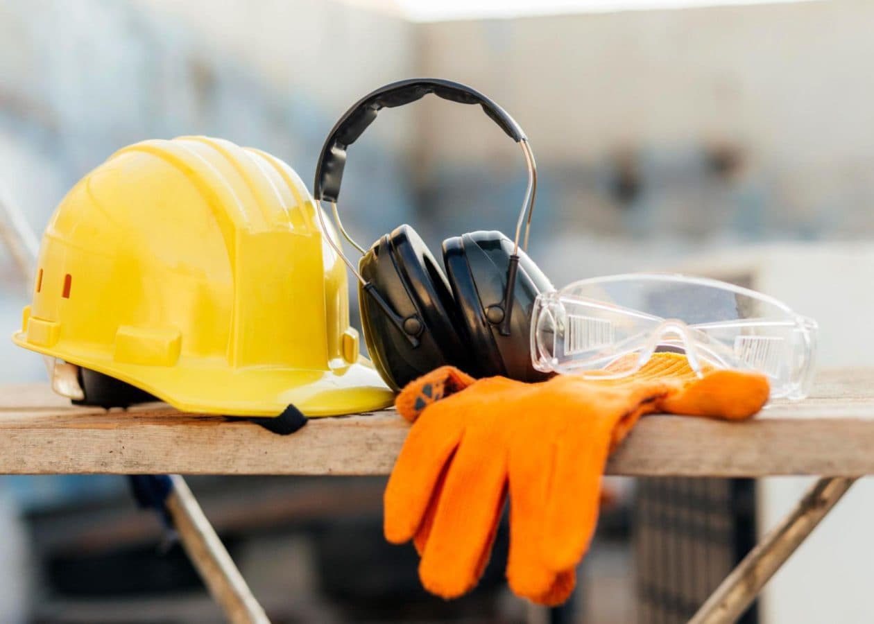 Yellow hard hat, earmuffs, goggles, and orange gloves for industrial safety
